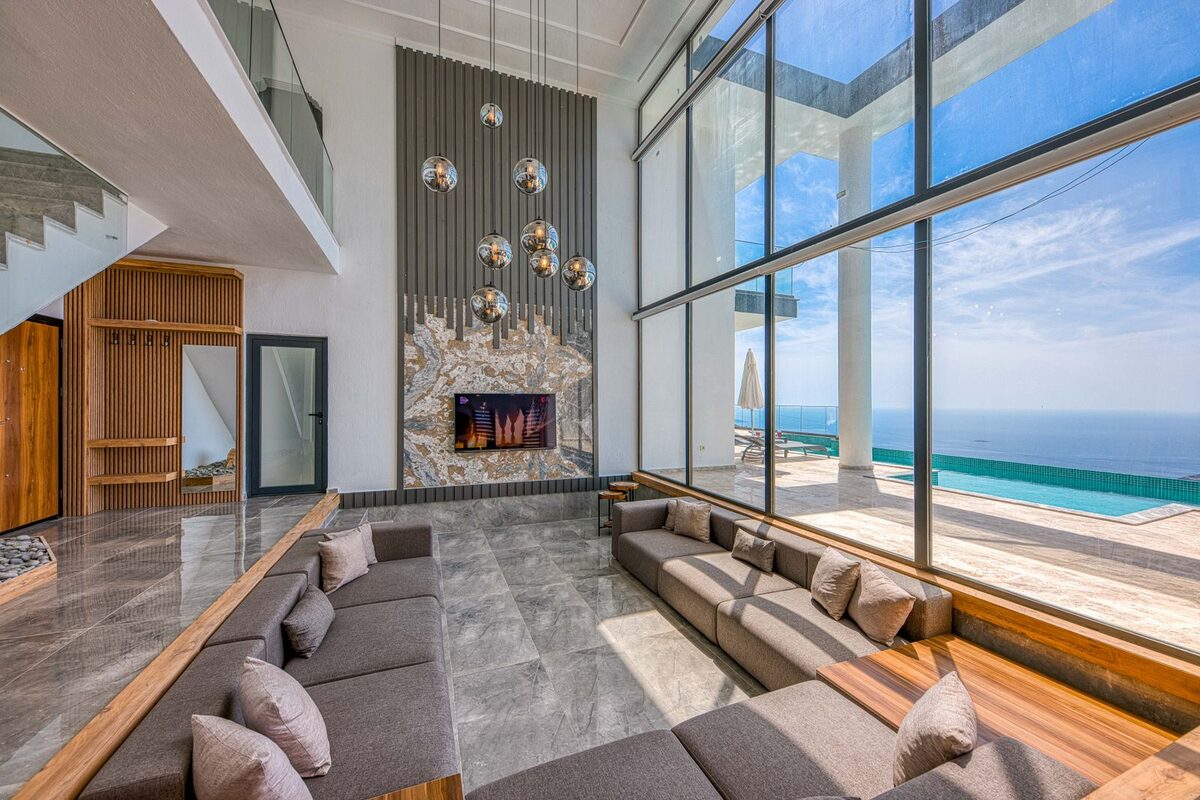 Double-height living room with floor-to-ceiling glass framing the ocean and a low fireplace
